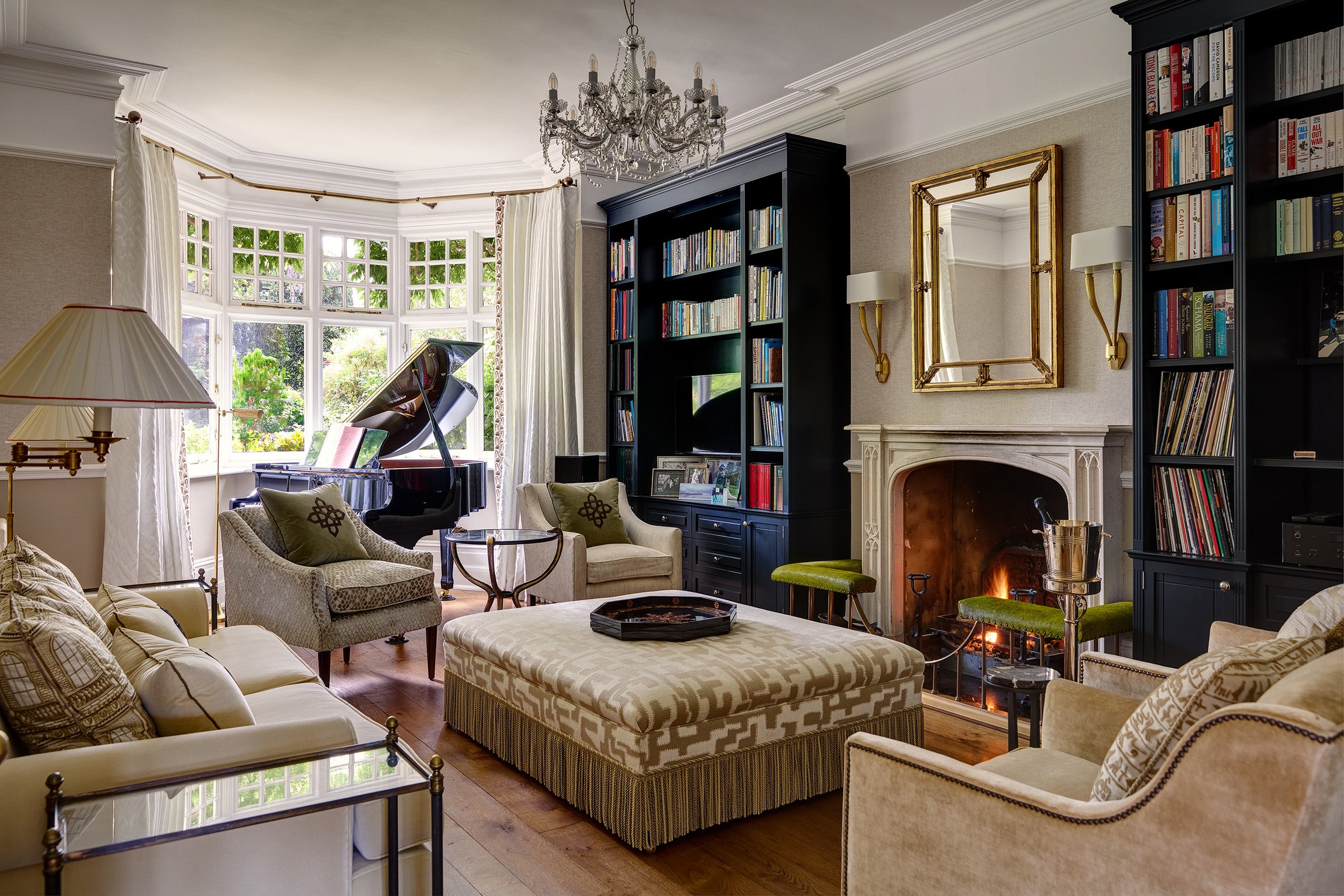 Luxurious living room with a grand piano, bookshelves, and a fireplace, and curtains in bay window.