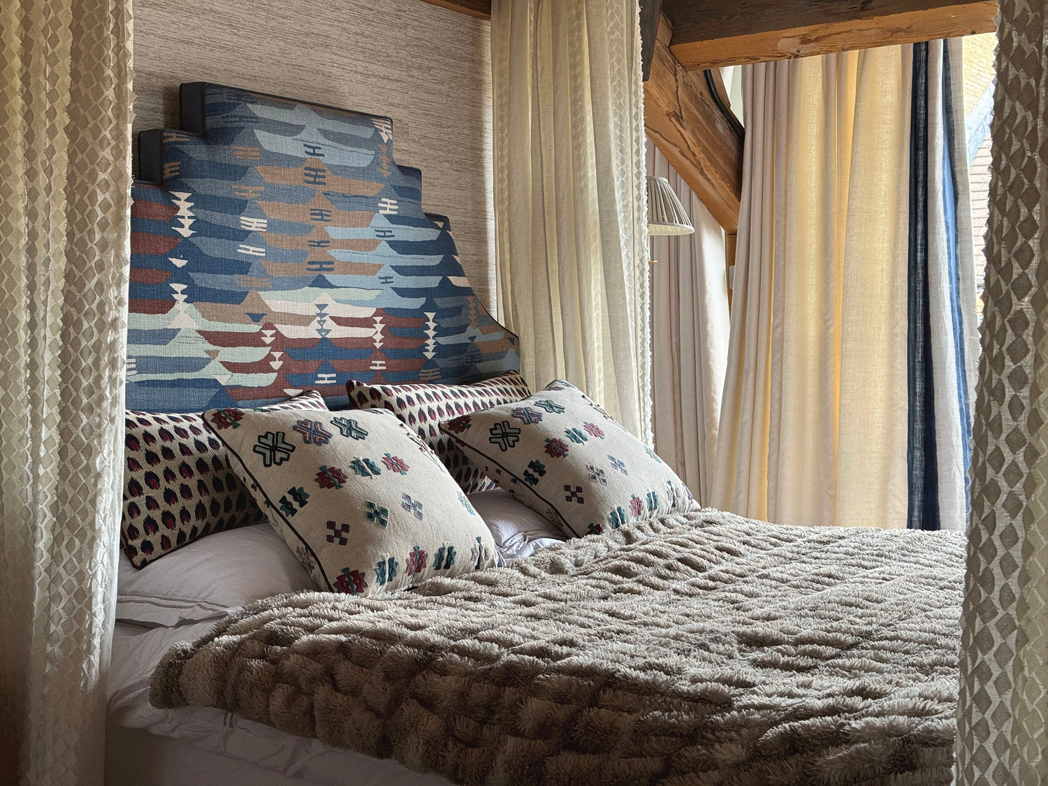 Bedroom with colourful patterned headboard and four poster embroidered bed curtains. Fabrics from Thibaut, Pierre Frey and Fabricut.