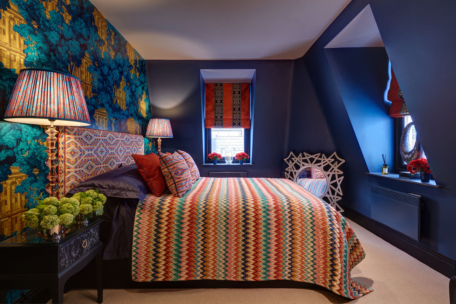 Opulent silk Roman blind in recess of deep navy and patterned wallpaper bedroom