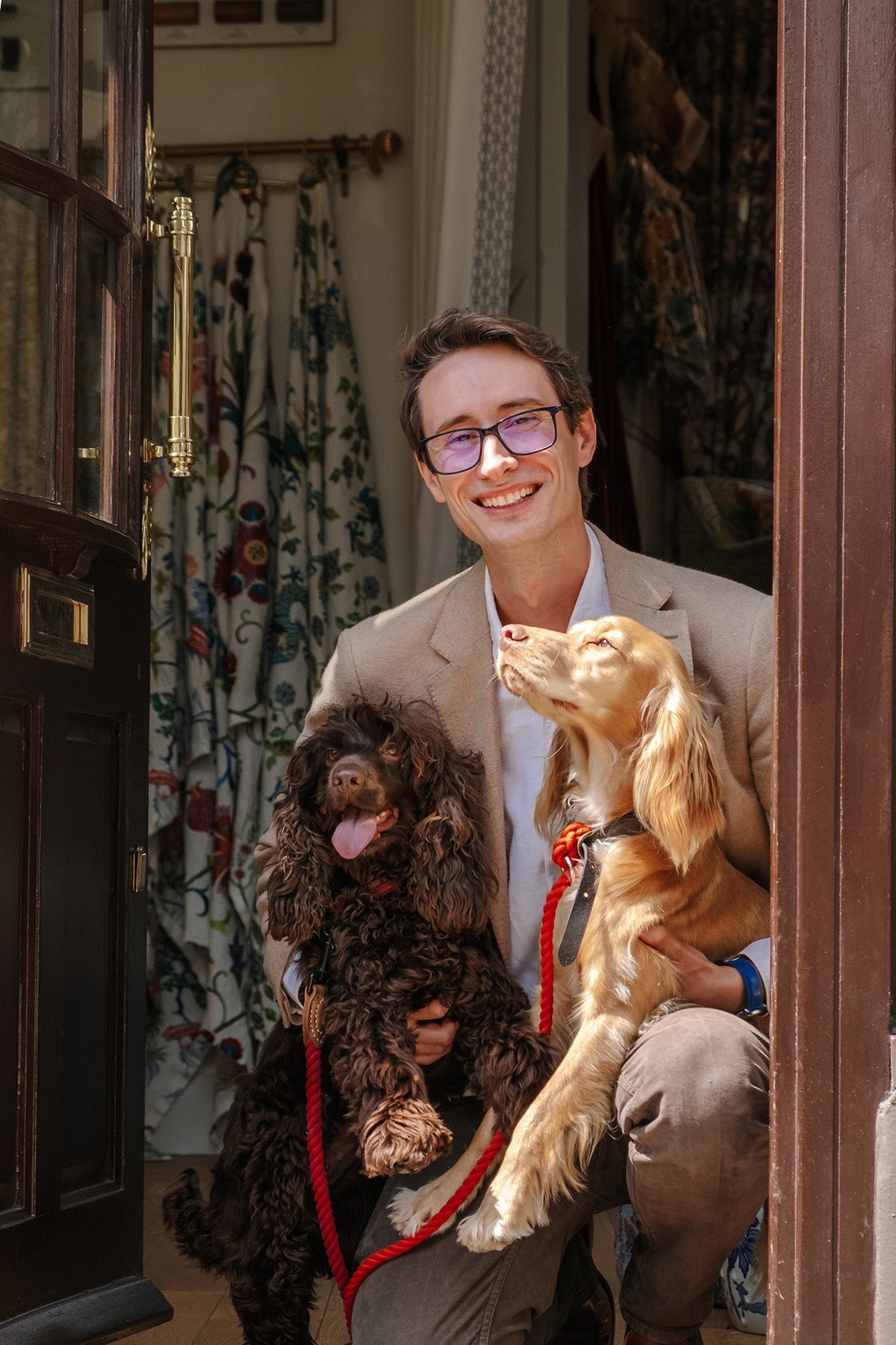 Man holding two dogs, one brown and one black, in a doorway.
